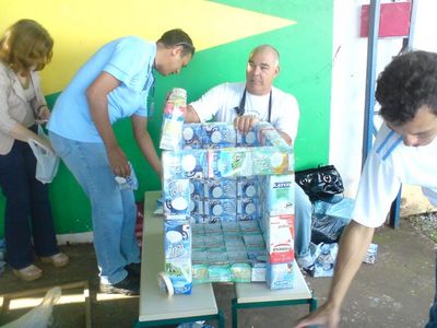 foto de pessoas trabalhando com as caixas de leite, colando-as para fazer o cho, a parede e o telhado da casinha de cachorro